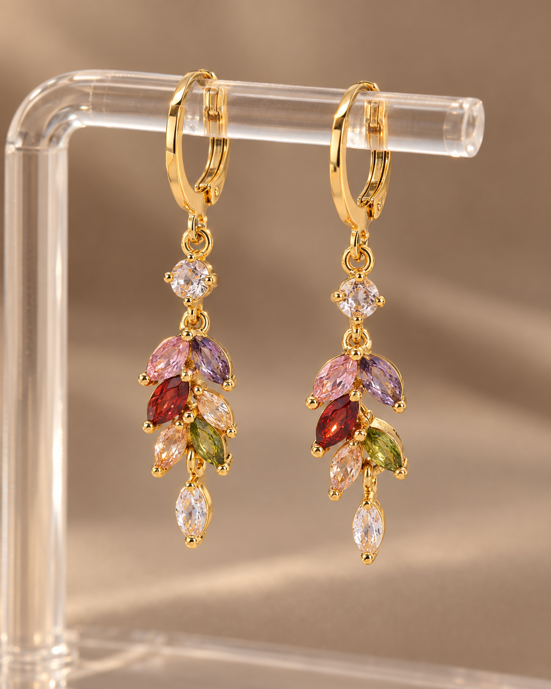 Pair of gold-tone multicolor zircon drop earrings on warm background