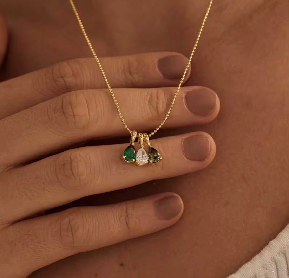 The Rosie gold birthstone necklace with three teardrop stones held by hand